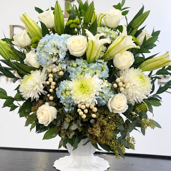 White roses, lilies, hydrangeas, and mums in a white pedestal vase