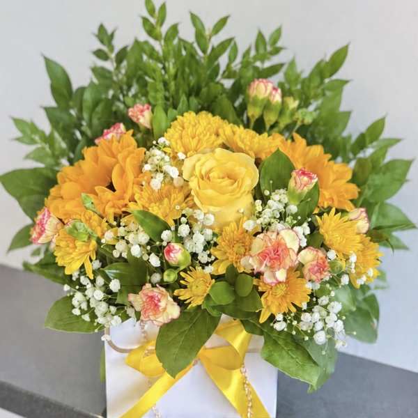 Yellow and orange flower arrangement in a white box with a yellow ribbon