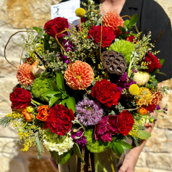 Large mixed bouquet in a glass vase with red, orange, and purple blooms