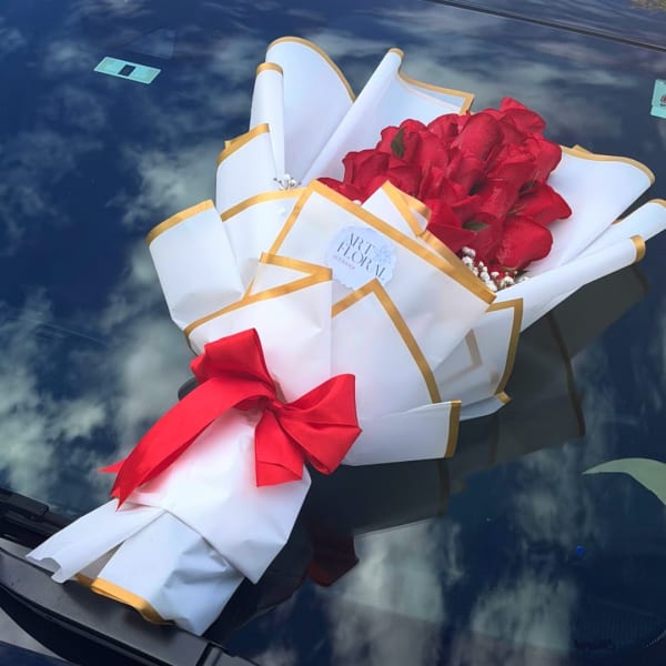 Bouquet of red roses wrapped in white paper with gold trim and a red bow