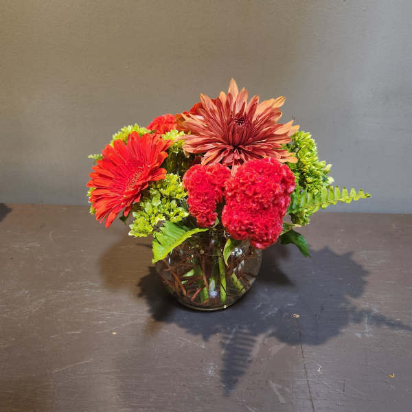 Mixed red and orange flowers in a round glass vase