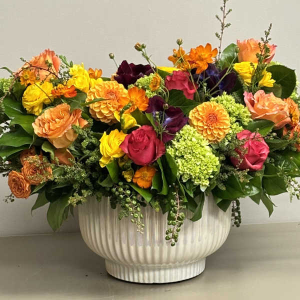 Low centerpiece of bright roses, dahlias, and green hydrangeas in a white ceramic bowl