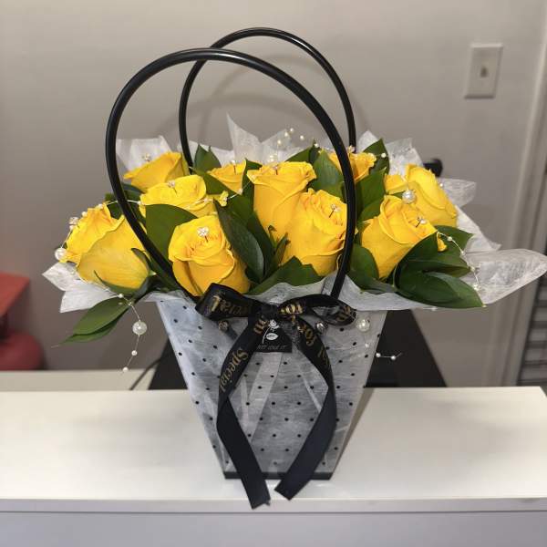 Yellow roses arranged in a black handled gift basket with ribbon