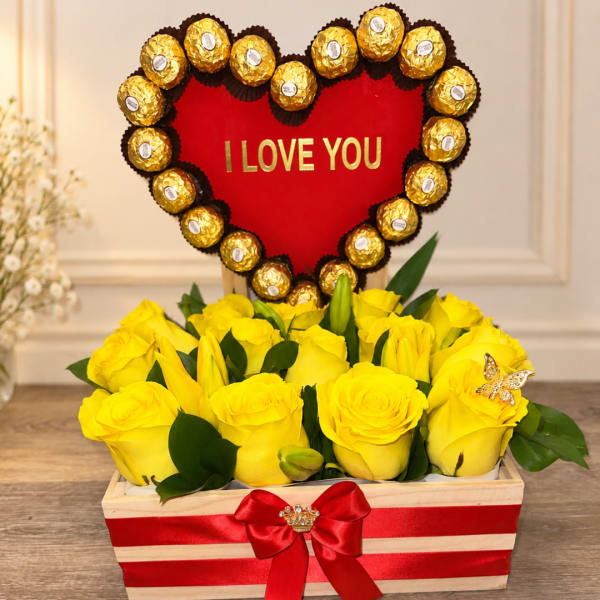 Yellow roses in a striped gift box with a heart-shaped chocolate topper