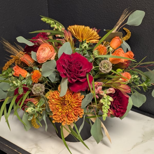 Mixed bouquet of red, orange, and peach flowers in a black vase