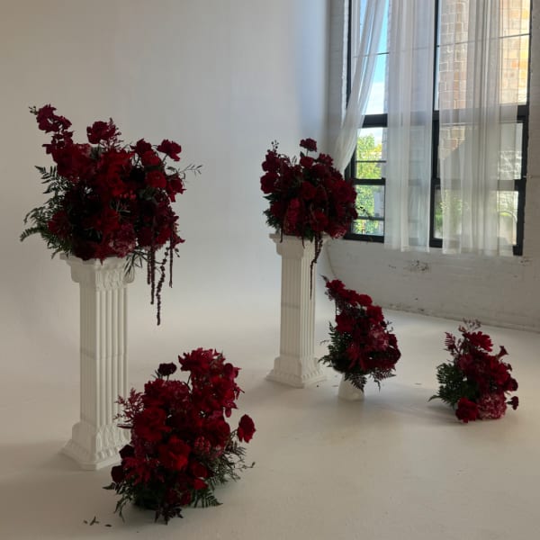 Deep red floral arrangements on white pedestals in a bright room