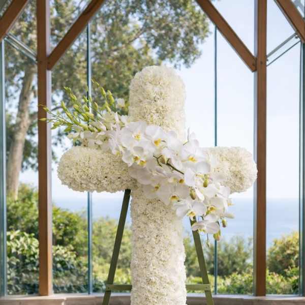 White floral cross on an easel with orchids and clustered blooms