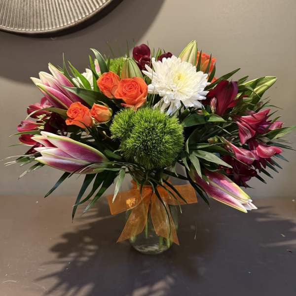 Mixed bouquet of orange roses, white chrysanthemum, and pink lilies in a glass vase