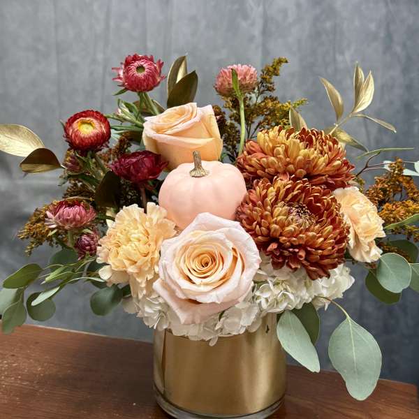 Mixed bouquet in a gold vase with roses, chrysanthemums, and a small pink pumpkin