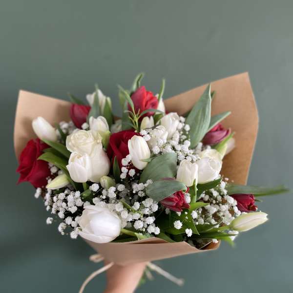 Handheld bouquet of red and white tulips wrapped in brown paper