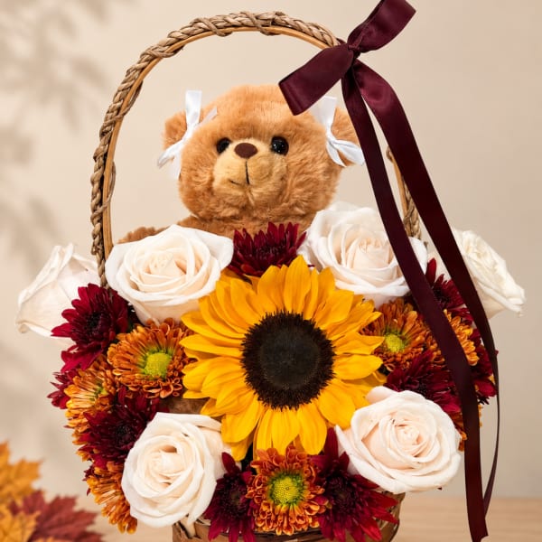 Teddy bear in a basket surrounded by roses, chrysanthemums, and a sunflower