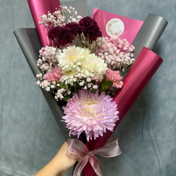 Handheld bouquet of pink, white, and burgundy flowers wrapped in magenta and black paper