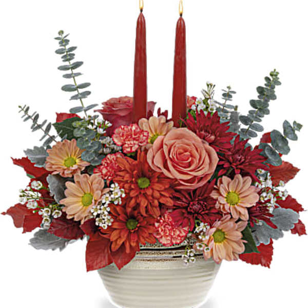 Red and peach floral arrangement with two red taper candles in a white bowl