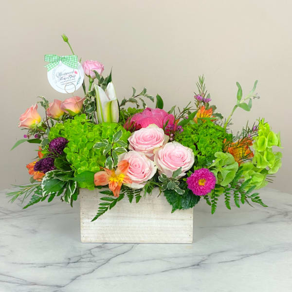 Mixed flower arrangement in a white wooden box with pink roses and bright green blooms