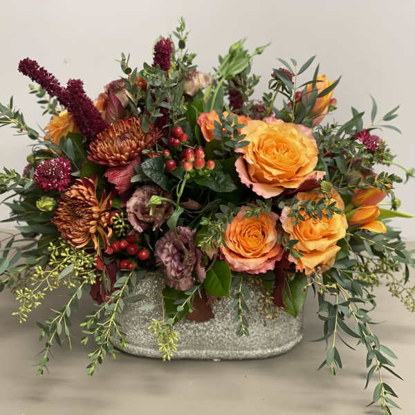 Low centerpiece of orange roses and rust mums with red accents in a gray ceramic container