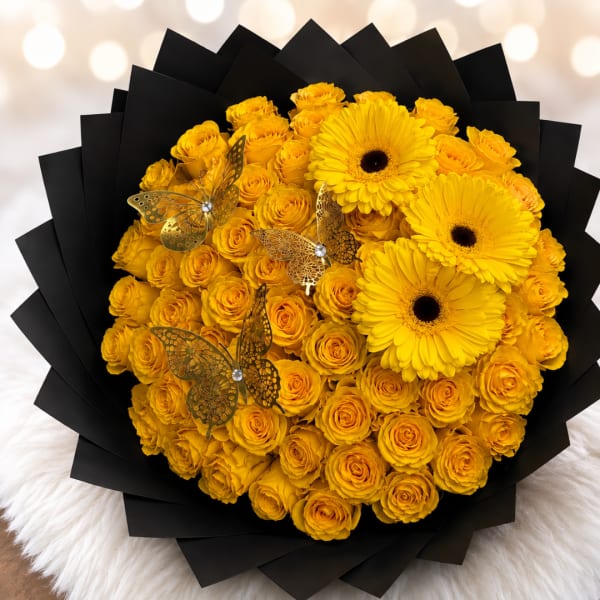 Yellow roses and gerbera daisies in black wrap with butterfly accents