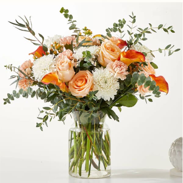 Peach roses and white mums in a clear glass vase
