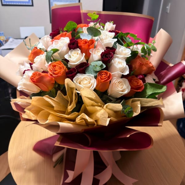 Bouquet of orange, white, and burgundy roses wrapped in burgundy and beige paper
