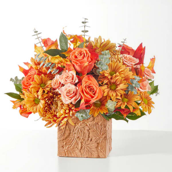 Orange and peach flowers in a leaf-patterned square vase