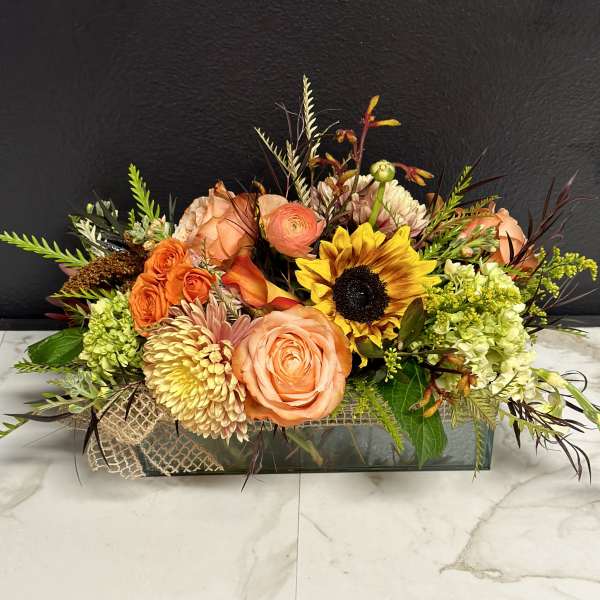 Mixed floral arrangement with peach roses and a sunflower in a low rectangular vase
