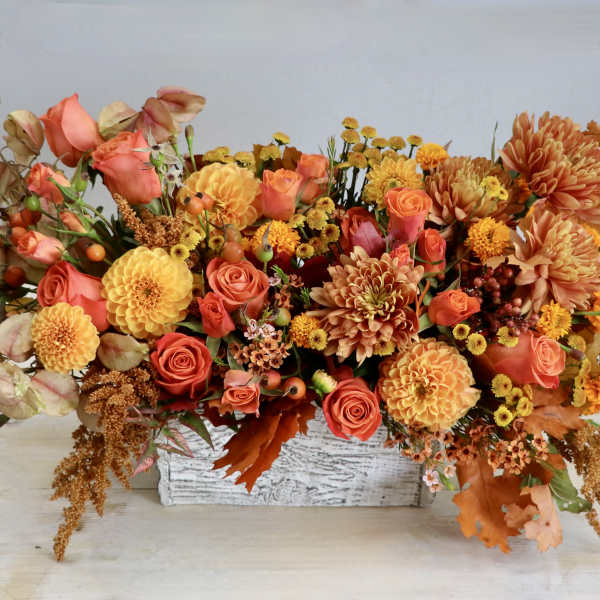 Low rectangular arrangement of orange and yellow roses, dahlias and mums in a white wood box.