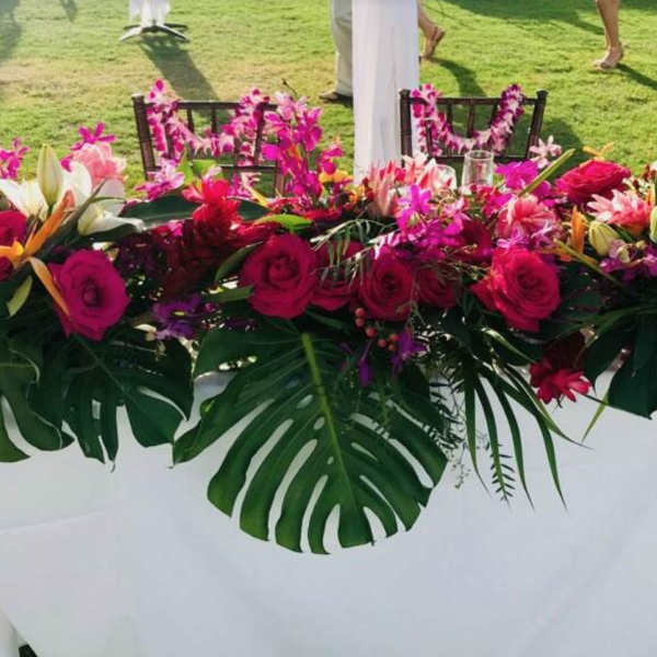 Long tropical floral centerpiece with pink roses and white lilies on a table