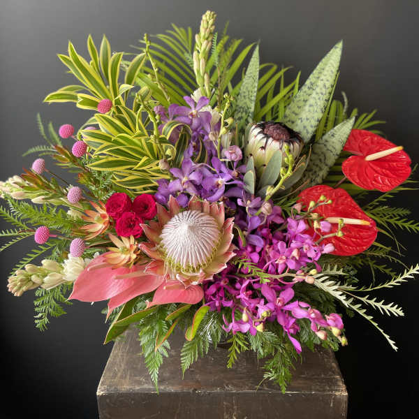 Tropical bouquet with purple orchids, red anthuriums, and a protea in a vase