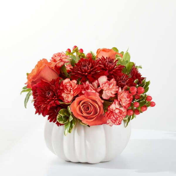 Orange roses and red flowers arranged in a white pumpkin vase