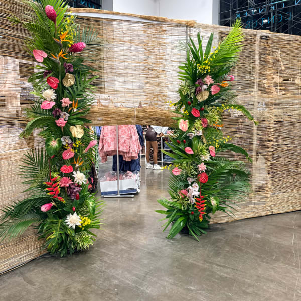 Two tall tropical floral columns frame a woven backdrop.