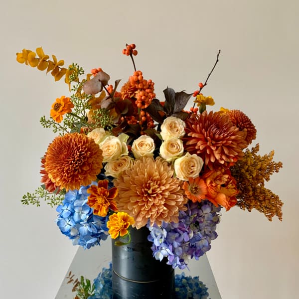 Autumn bouquet with orange chrysanthemums, cream roses, and blue hydrangeas in a black vase