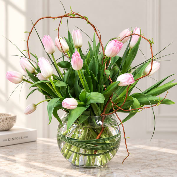 Pink tulips arranged in a clear glass bowl vase with curly branches