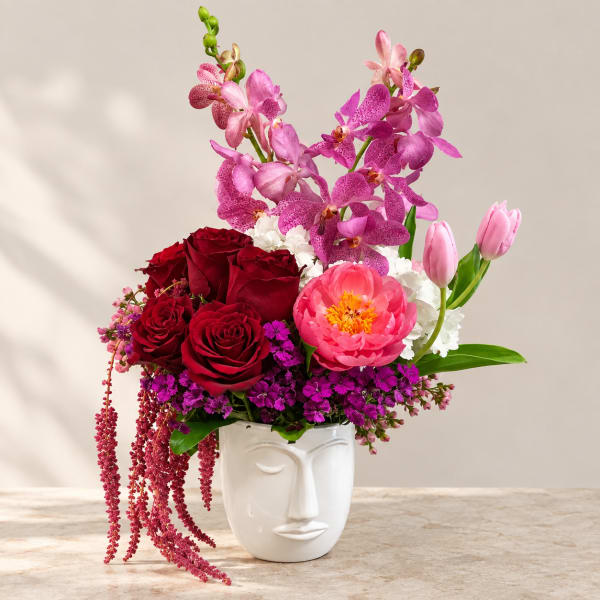 Mixed bouquet in a white face vase with pink orchids, red roses, and tulips