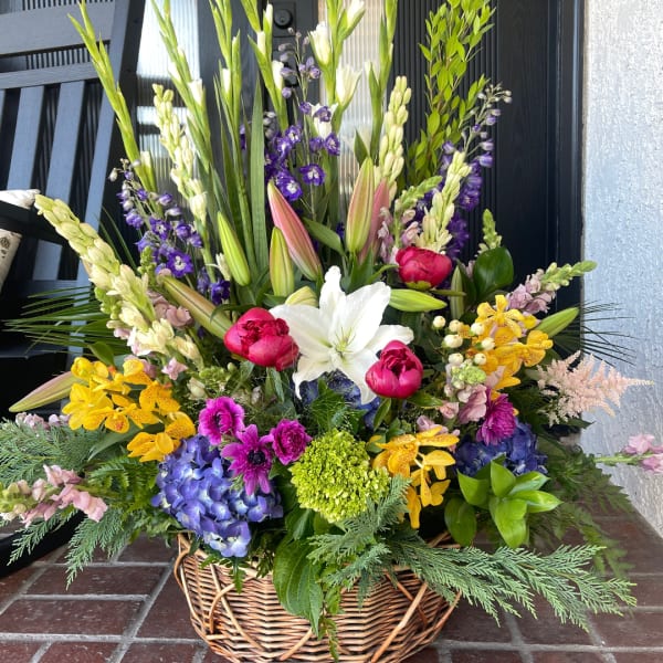 Large mixed flower arrangement in a wicker basket with lilies, orchids, and hydrangea