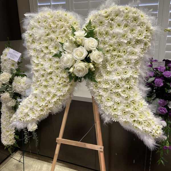 White floral heart-shaped standing spray with roses and daisies on an easel
