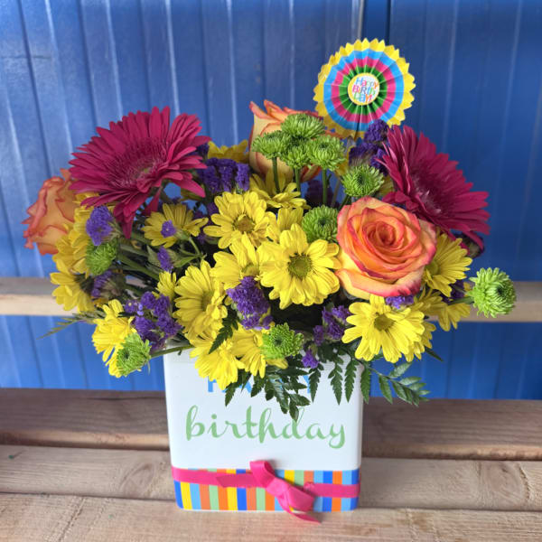 Bright mixed flower arrangement in a birthday gift box with a colorful topper