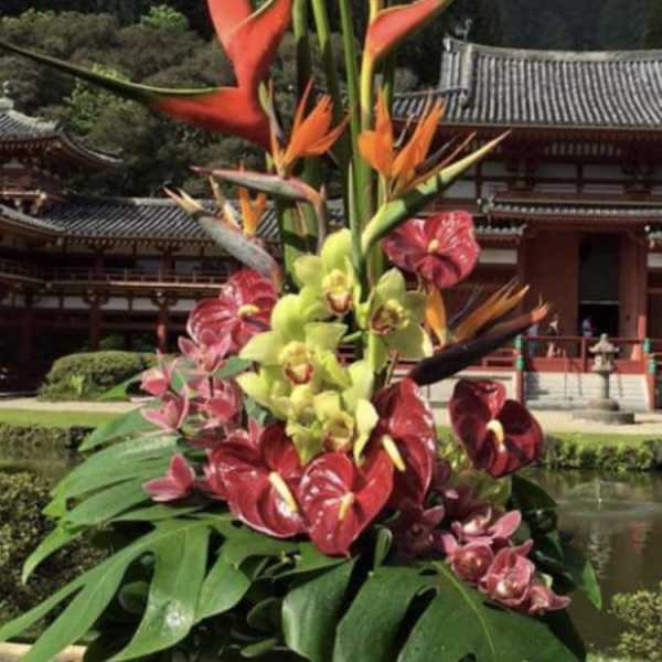 Tropical flower arrangement with orange heliconia and orchids in a white vase