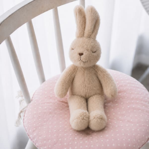 Plush beige bunny sitting on a pink polka-dot cushion on a white chair