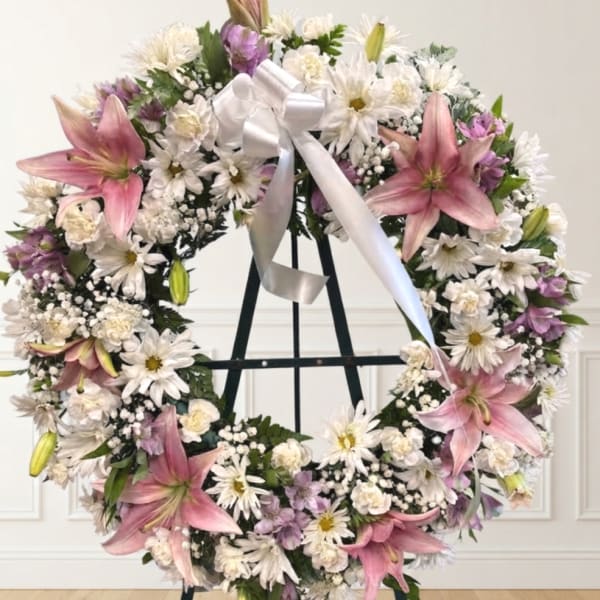 Large floral wreath with pink lilies, white daisies, and a white ribbon on an easel
