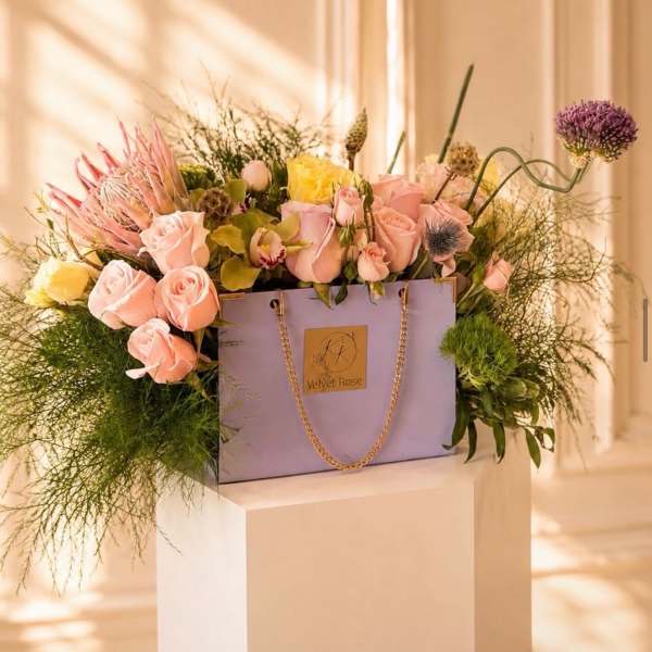 Lavender gift bag filled with pink and yellow roses and mixed blooms