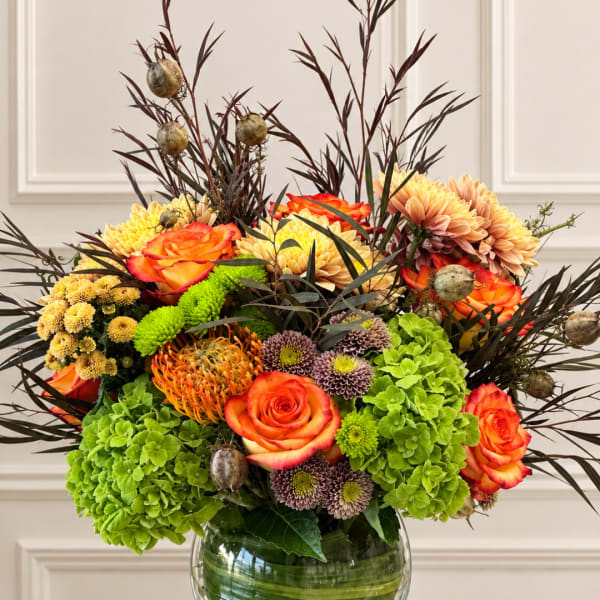 Mixed bouquet of orange roses, chrysanthemums, and green hydrangeas in a glass vase