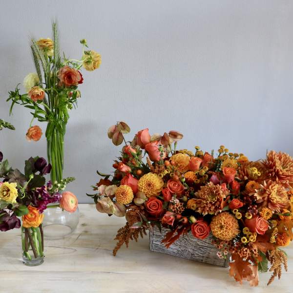 Set of orange and yellow mixed flower arrangements in glass vases and a rustic rectangular container