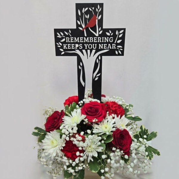 Red and white sympathy arrangement beneath a memorial cross sign