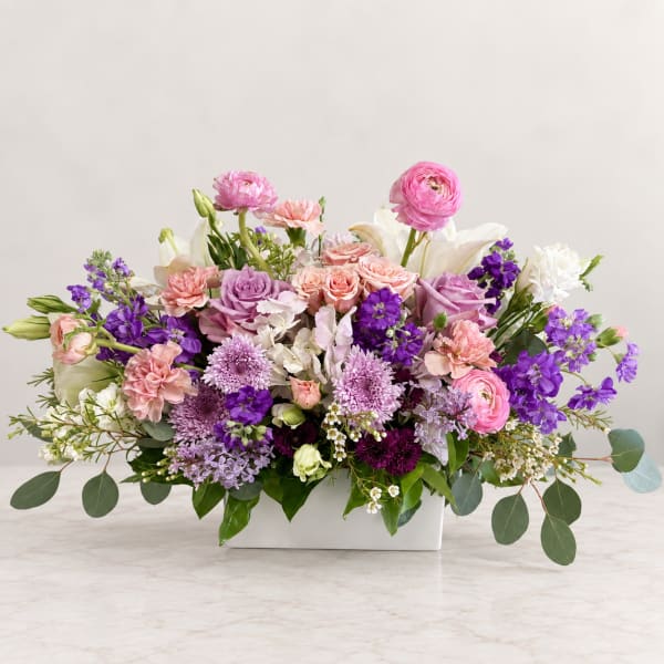 Mixed pink, purple, and white flowers arranged in a white rectangular vase