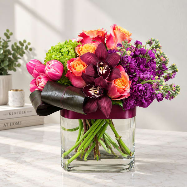 Colorful bouquet of roses, orchids, and tulips in a clear glass vase