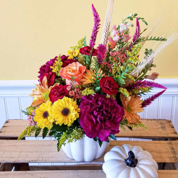 Colorful flower arrangement in a white pumpkin-shaped vase with a small white pumpkin decor piece nearby.