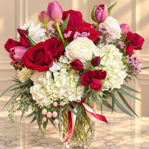 Red roses and white blooms in a glass vase with pink tulips