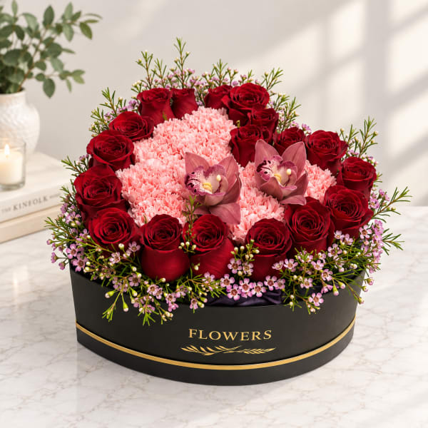 Round box arrangement of red roses, pink carnations, and orchids