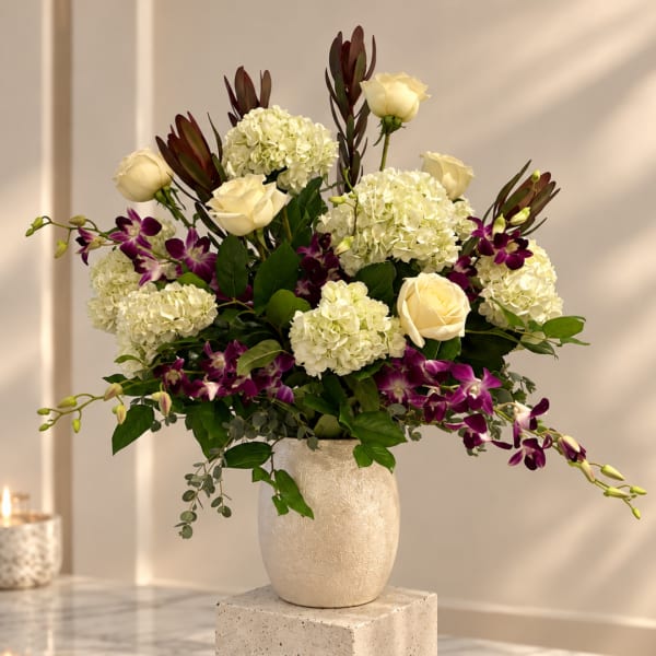 Cream roses and white hydrangeas in a textured vase with purple orchids
