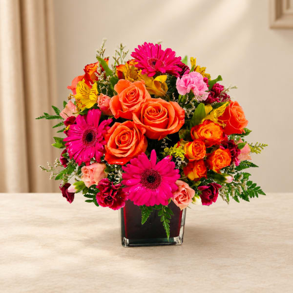 Bright mixed bouquet of roses and gerbera daisies in a square glass vase
