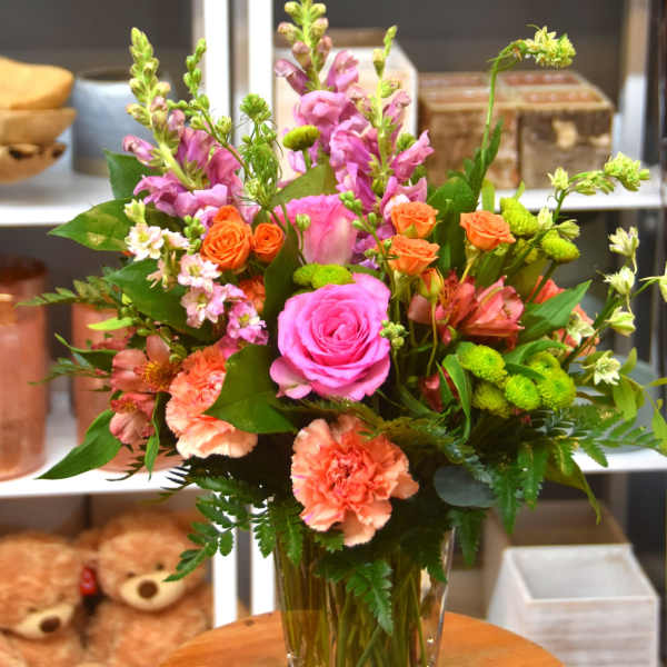 Tall mixed bouquet with pink roses, peach carnations, and orange spray roses in a clear glass vase
